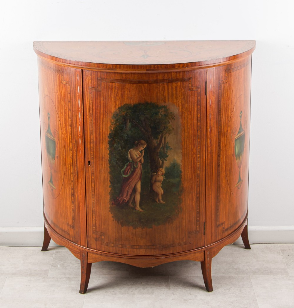 A late Victorian satinwood demi-lune side cabinet featuring hand-painted classical figures and urn panels on tapered legs. View II