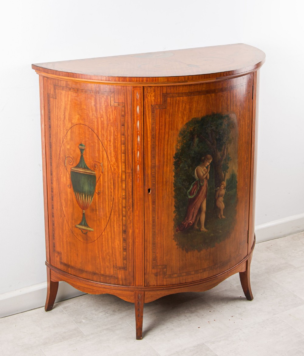 A late Victorian satinwood demi-lune side cabinet featuring hand-painted classical figures and urn panels on tapered legs. View III