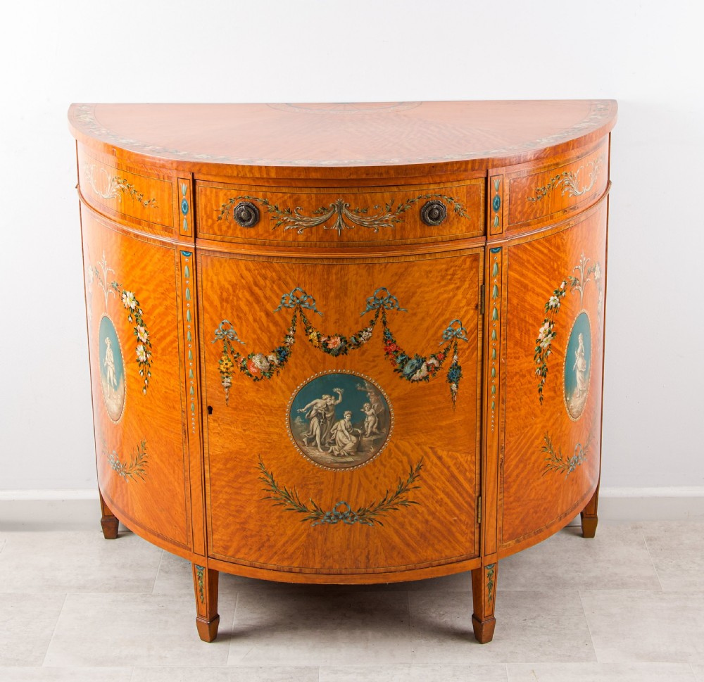 An Edwardian satinwood demi-lune commode with hand-painted classical vignettes, floral garlands, and square tapered legs. View II