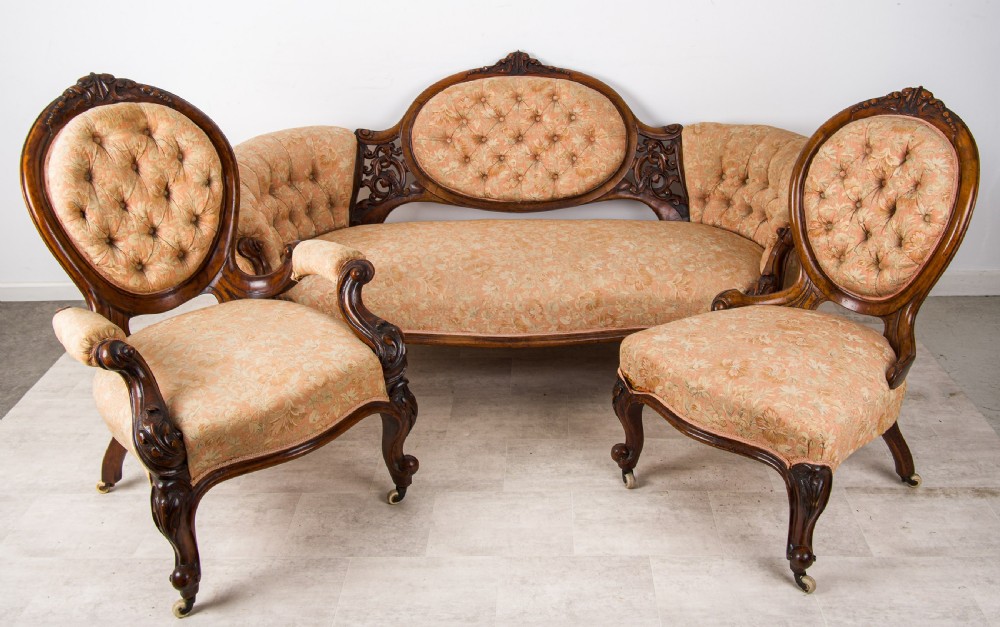 An antique Victorian three-piece seating suite featuring a carved walnut settee and two matching armchairs upholstered in peach damask fabric with button-tufted backs and cabriole legs.