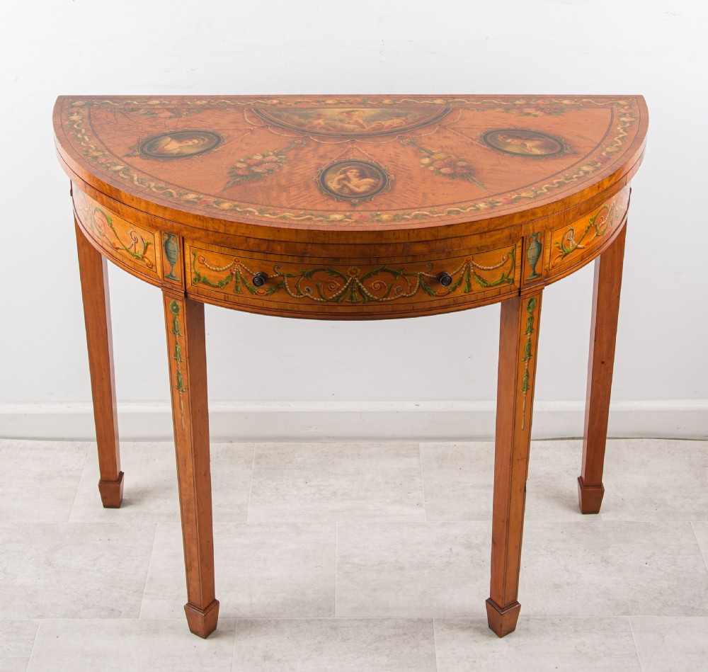 A nineteenth-century demi-lune satinwood card table featuring hand-painted classical portrait medallions, floral swags, and square tapered legs.