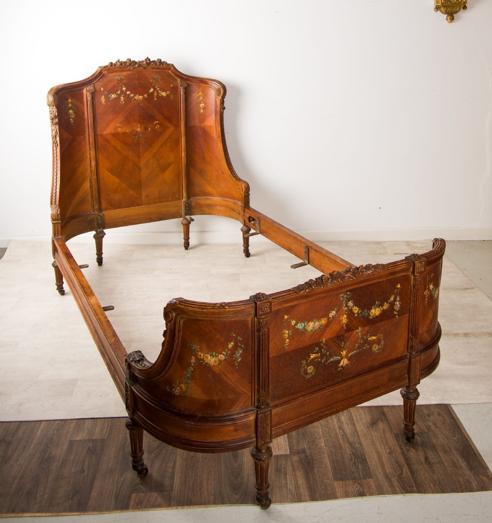 An antique French wooden bed frame featuring a high curved headboard, wrapped footboard, parquetry veneer, and hand-painted floral swags. View III