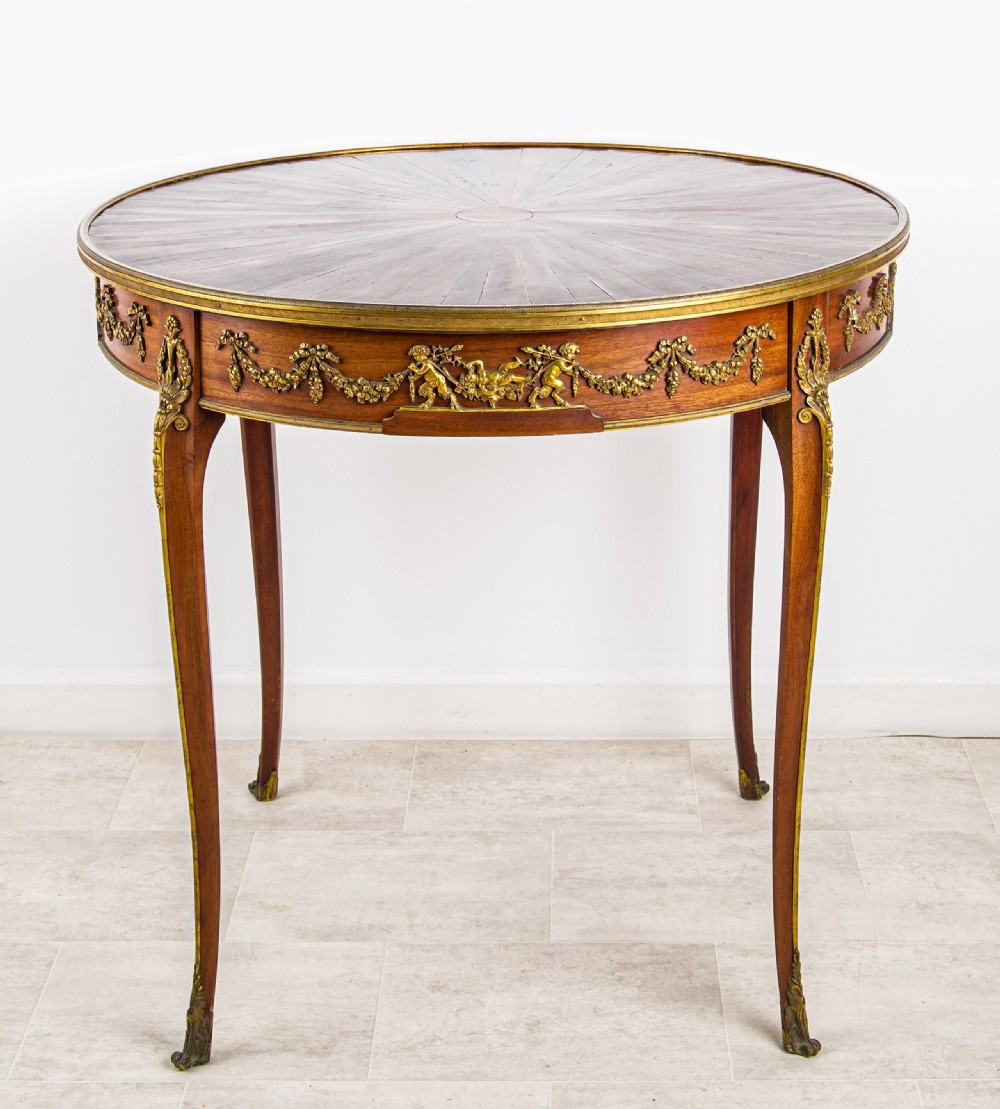 A circular French centre table featuring a sunburst marquetry veneer top, slender cabriole legs, and ornate gilt bronze mounts around the apron.
