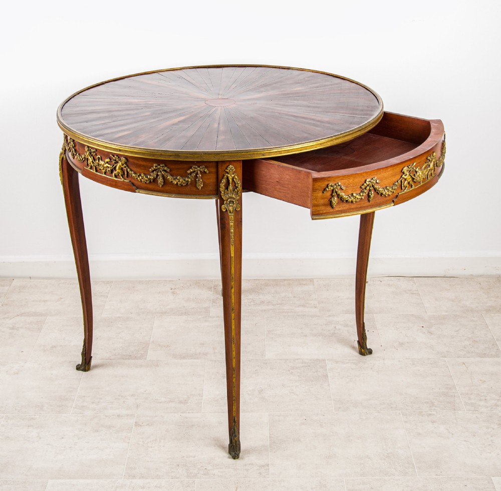A circular French centre table featuring a sunburst marquetry veneer top, slender cabriole legs, and ornate gilt bronze mounts around the apron. View VI