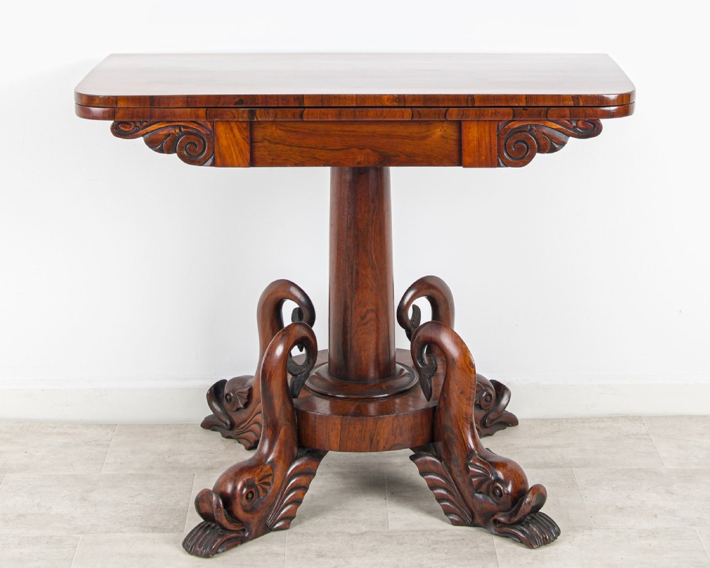 A Regency rosewood games table featuring a swivel fold-over rectangular top set above a central pedestal with four carved dolphin-form feet. View III