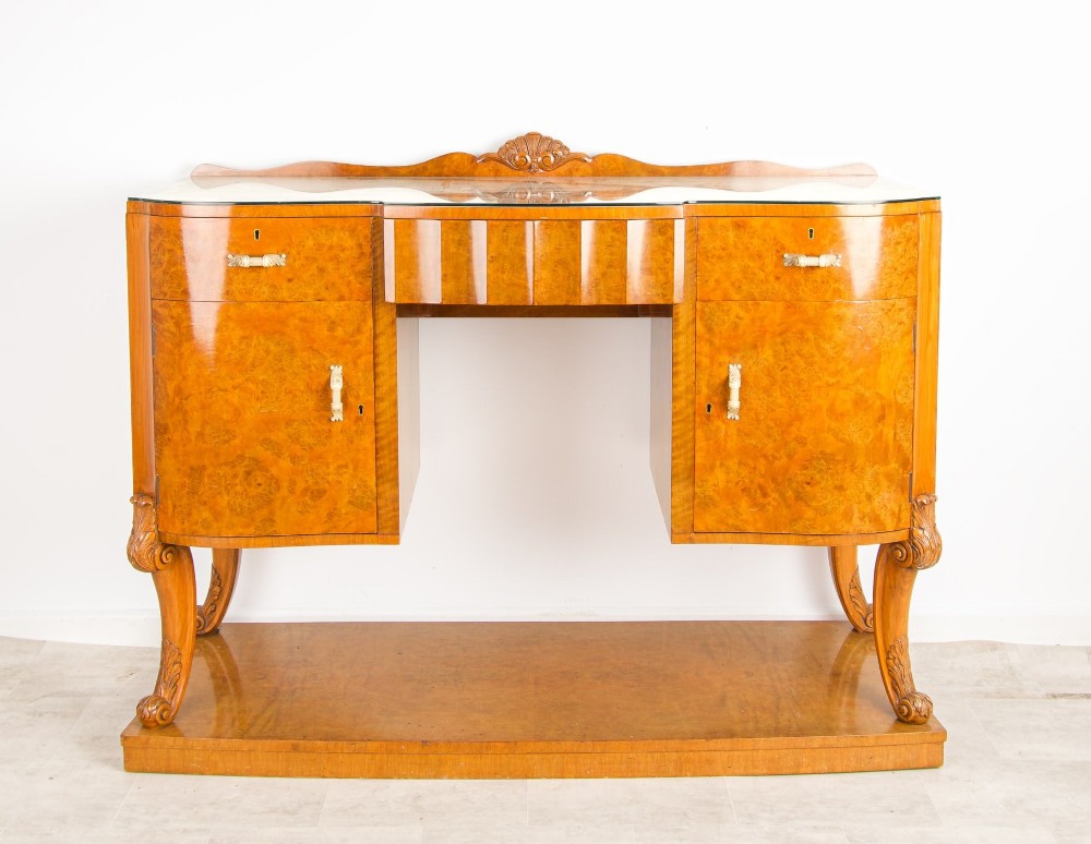 An Art Deco burr walnut sideboard featuring two outer pedestal cupboards, carved cabriole legs, a glass top, and a lower plinth base. View II