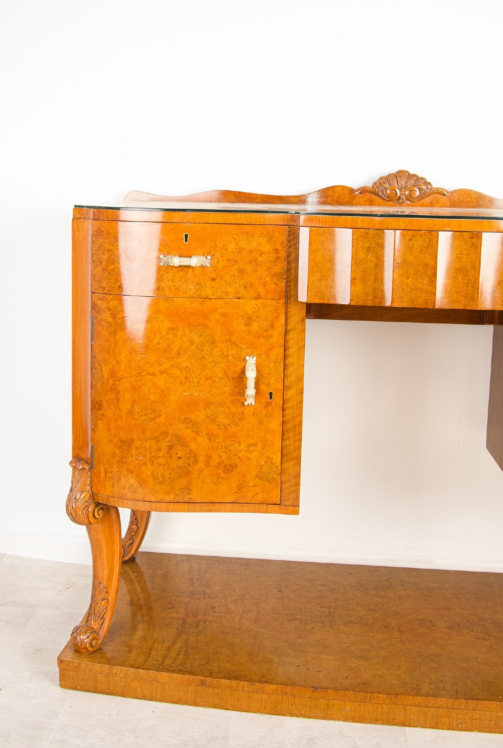 An Art Deco burr walnut sideboard featuring two outer pedestal cupboards, carved cabriole legs, a glass top, and a lower plinth base. View III