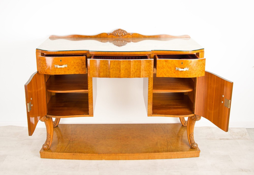 An Art Deco burr walnut sideboard featuring two outer pedestal cupboards, carved cabriole legs, a glass top, and a lower plinth base. View V