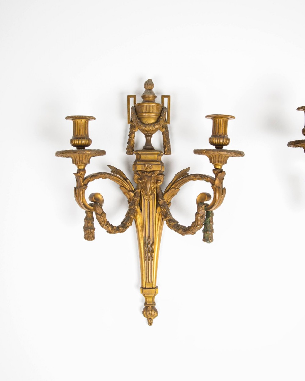 A pair of 19th-century French Neoclassical gilt bronze two-arm wall sconces featuring urn finials, rams head masks, fluted central shafts, and drapery swags. View II