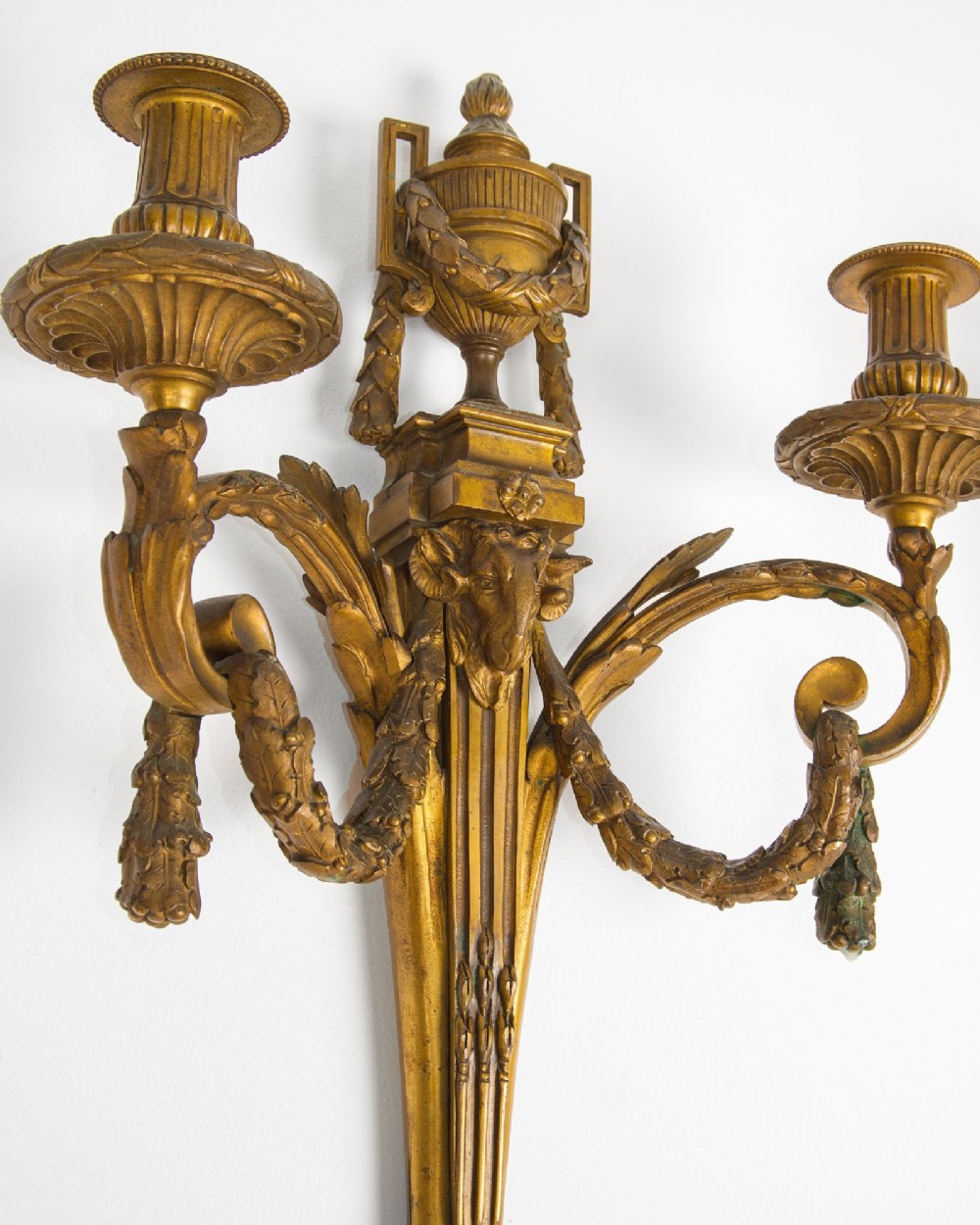 A pair of 19th-century French Neoclassical gilt bronze two-arm wall sconces featuring urn finials, rams head masks, fluted central shafts, and drapery swags. View IV