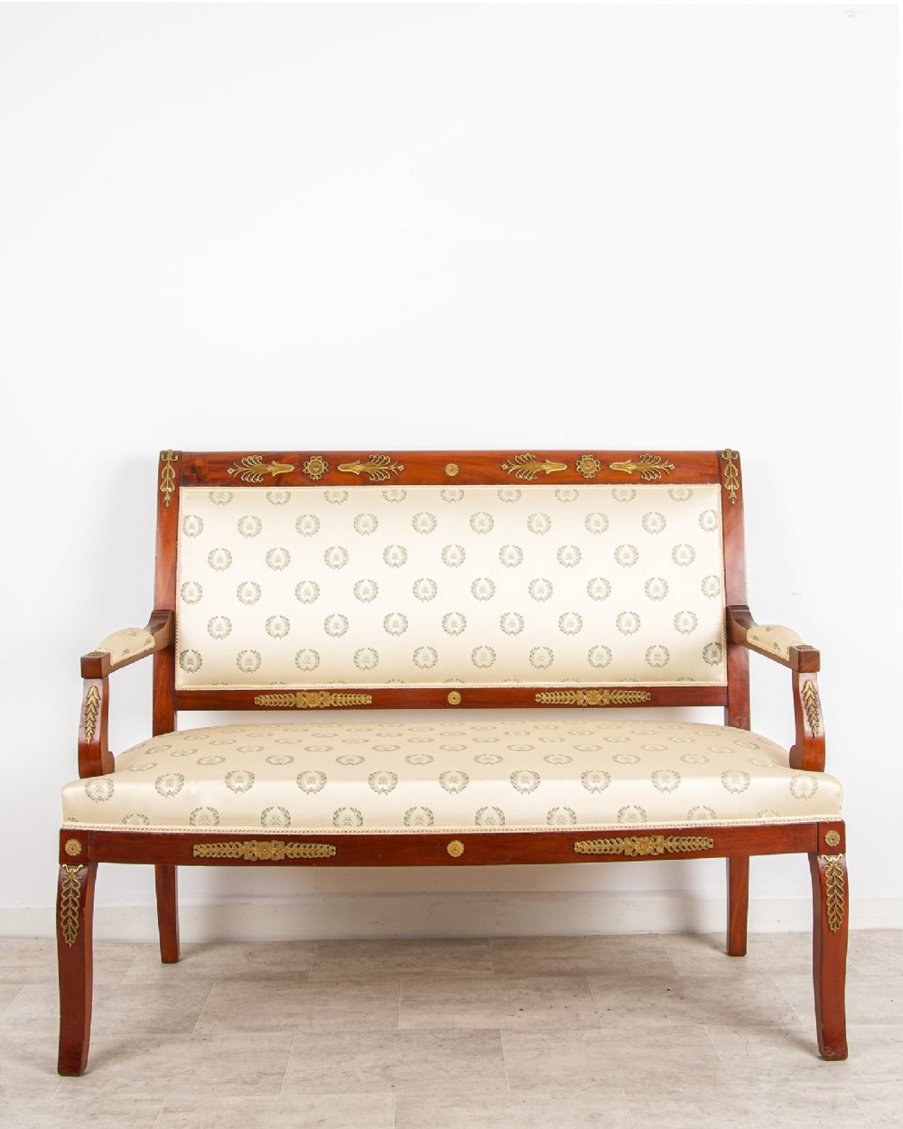 A French Empire Revival mahogany settee with cream patterned silk upholstery, curved arms, and gilded metal ormolu mounts.