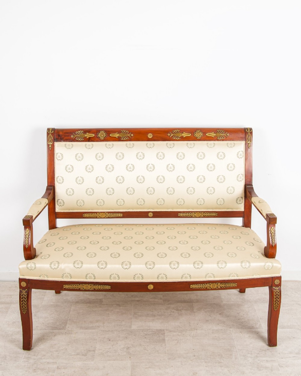 A French Empire Revival mahogany settee with cream patterned silk upholstery, curved arms, and gilded metal ormolu mounts. View II