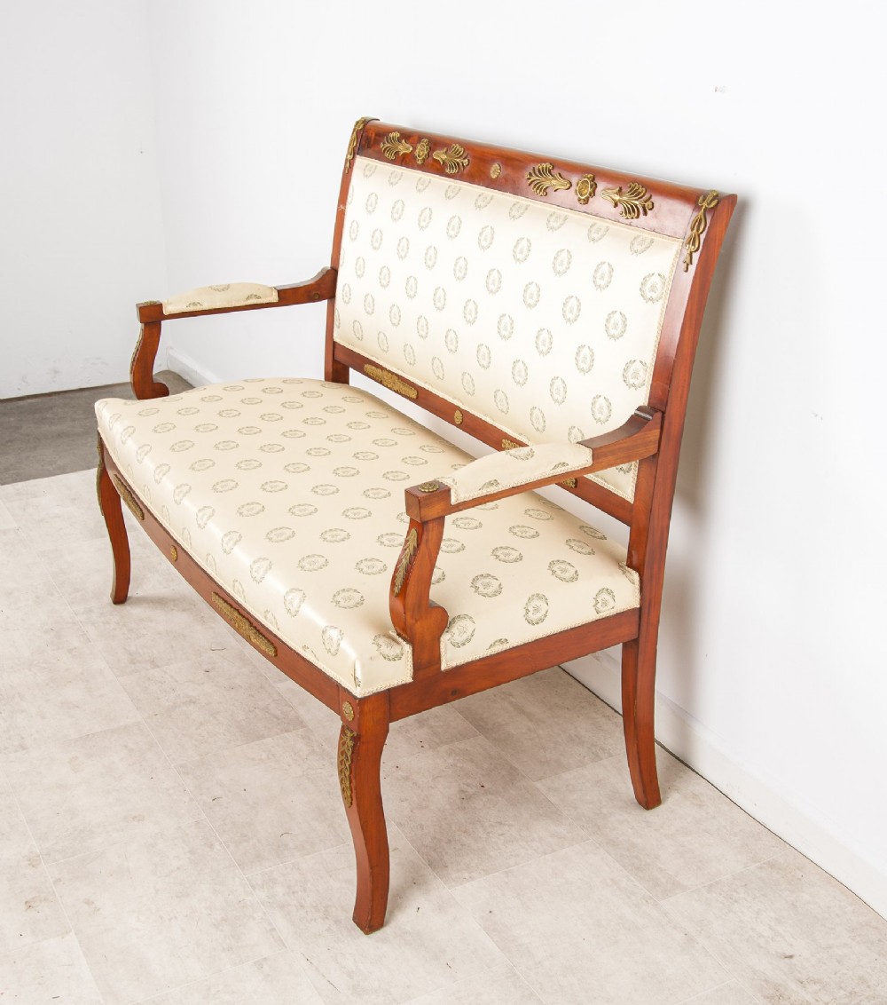 A French Empire Revival mahogany settee with cream patterned silk upholstery, curved arms, and gilded metal ormolu mounts. View V