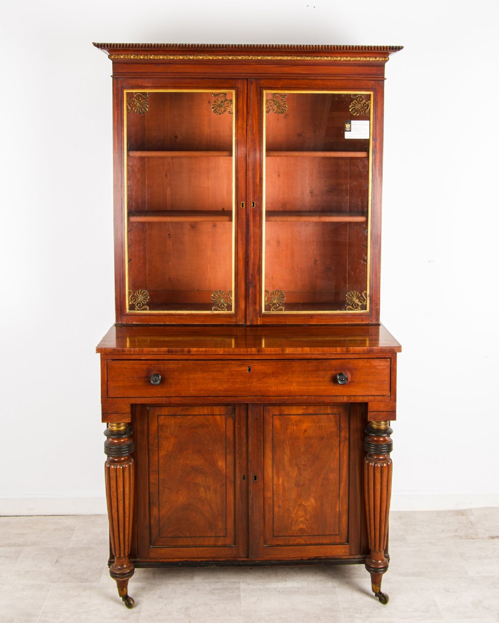 An antique Regency mahogany glazed bookcase cabinet with brass decorative mounts, fluted columns, and a lower two-door cupboard. View II