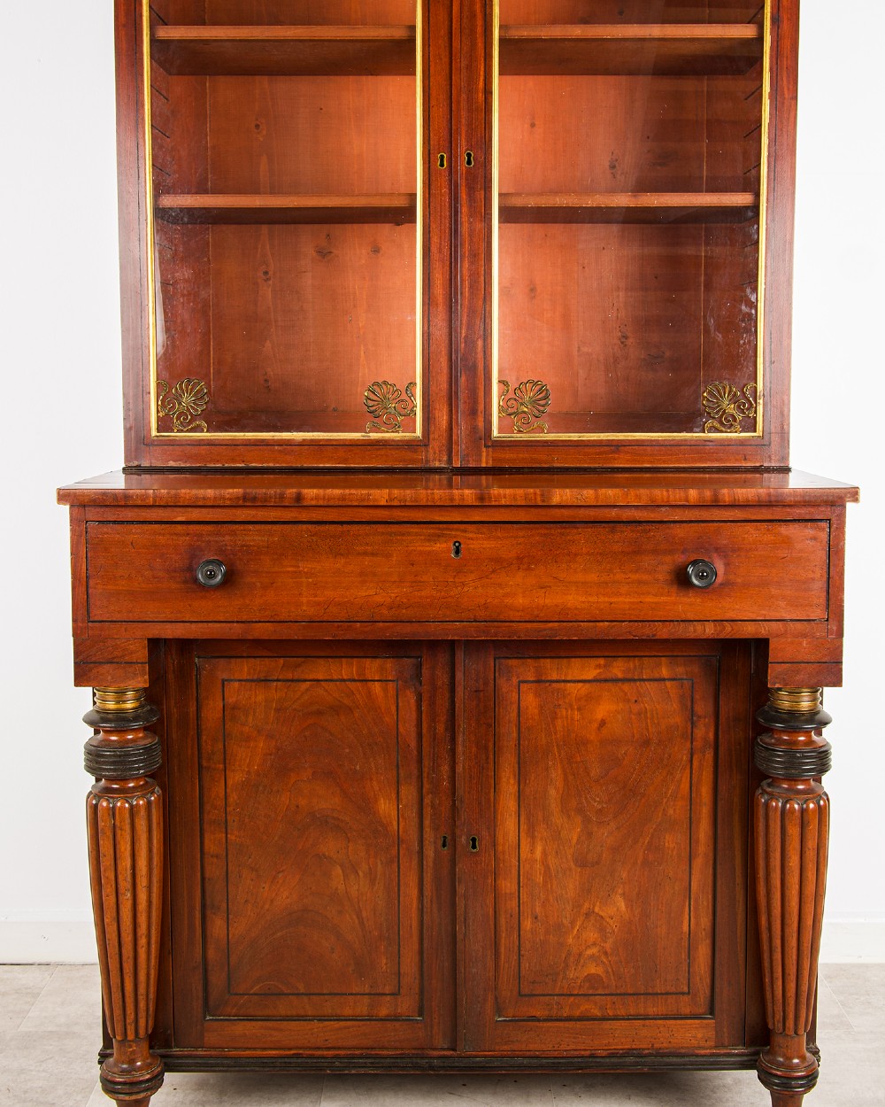 An antique Regency mahogany glazed bookcase cabinet with brass decorative mounts, fluted columns, and a lower two-door cupboard. View III