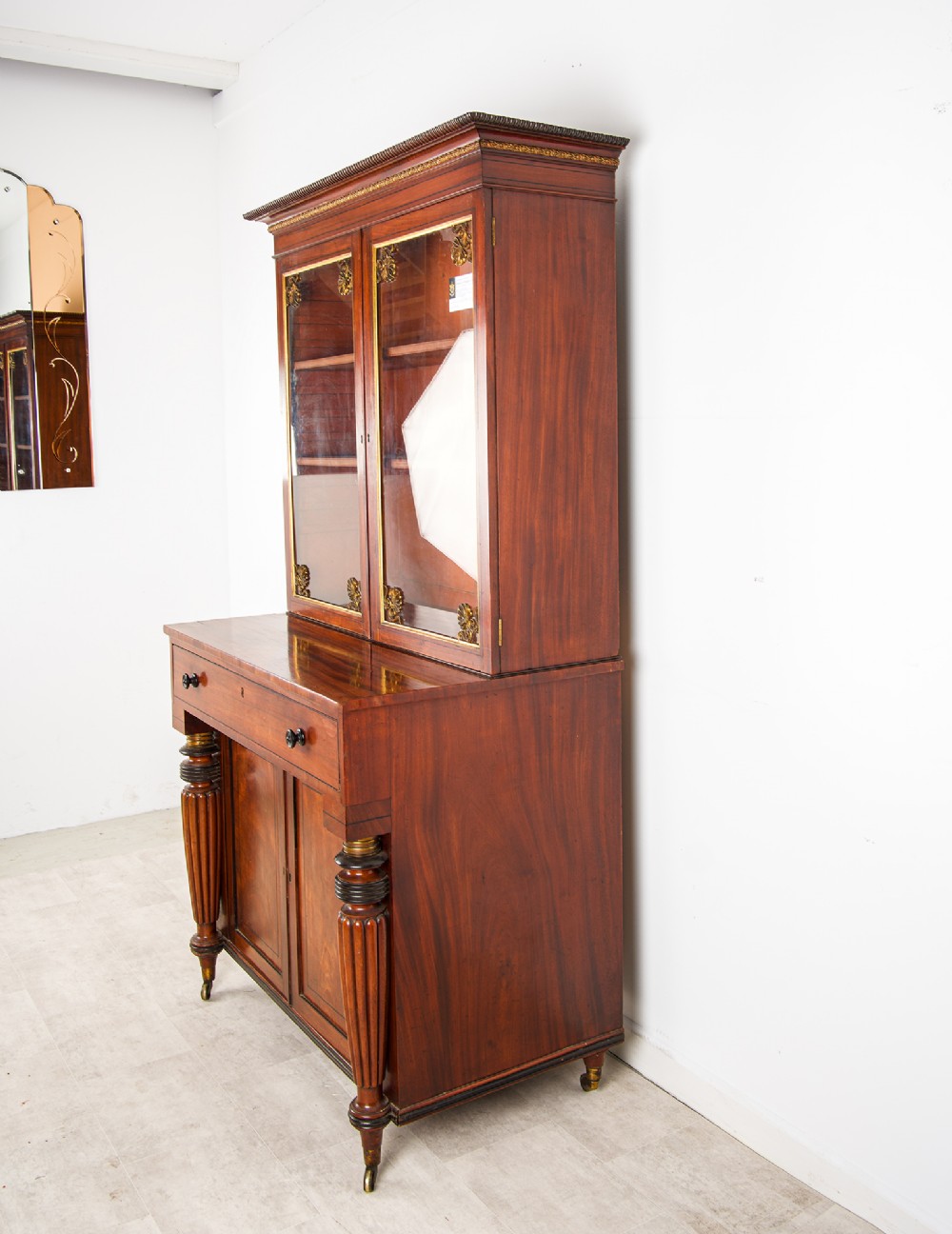 An antique Regency mahogany glazed bookcase cabinet with brass decorative mounts, fluted columns, and a lower two-door cupboard. View VI
