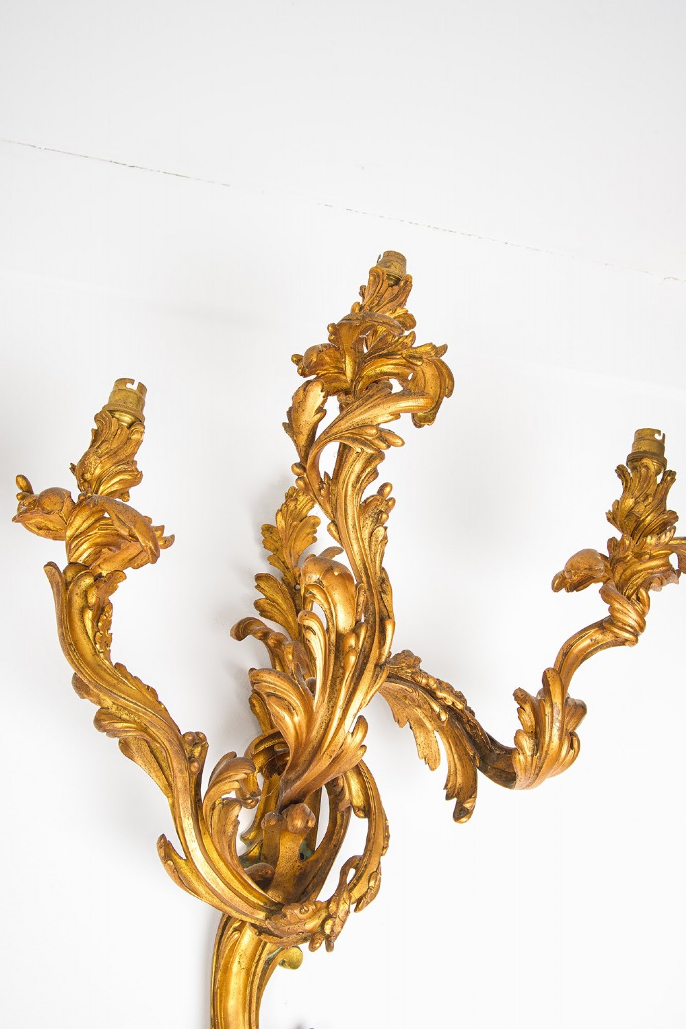 A pair of gilt bronze French ormolu three-branch wall lights decorated with sweeping Rococo acanthus leaf scrollwork. View VII
