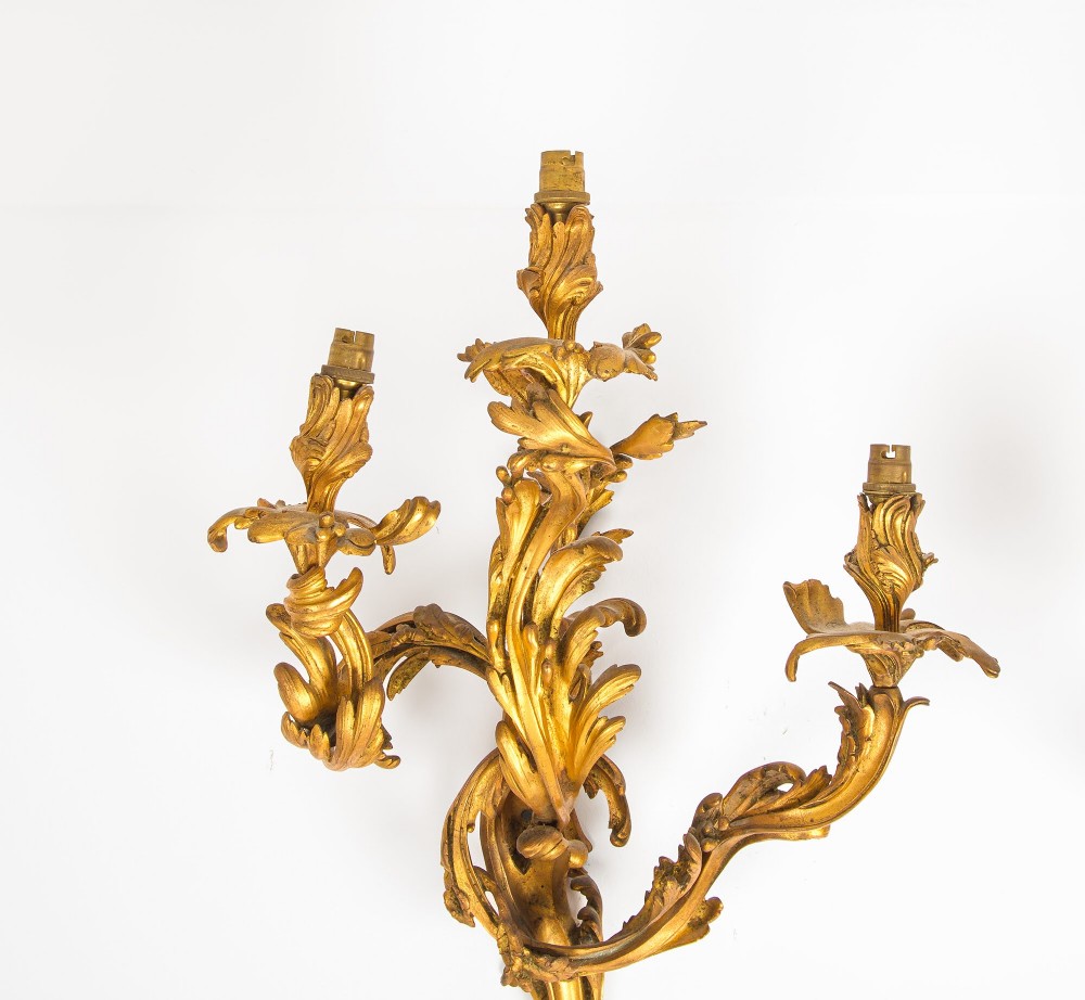 A pair of gilt bronze French ormolu three-branch wall lights decorated with sweeping Rococo acanthus leaf scrollwork. View X