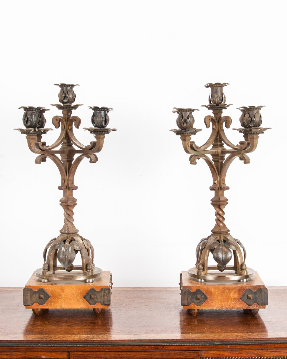 A pair of five-branch Gothic Revival metal candelabra featuring foliate cups, twisted columns, and wooden bases with iron strapwork.