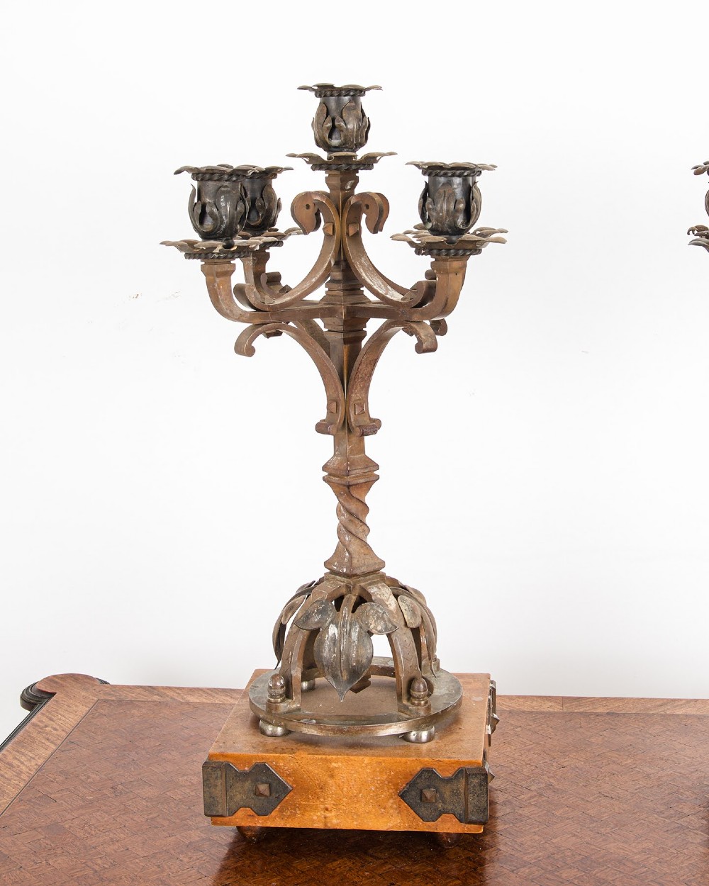 A pair of five-branch Gothic Revival metal candelabra featuring foliate cups, twisted columns, and wooden bases with iron strapwork. View II