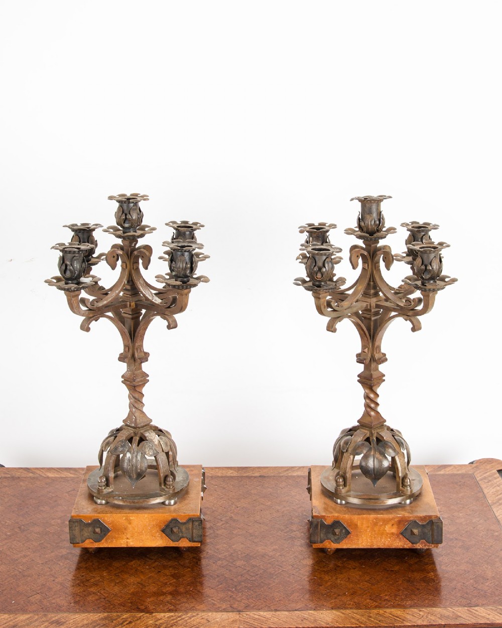 A pair of five-branch Gothic Revival metal candelabra featuring foliate cups, twisted columns, and wooden bases with iron strapwork. View III