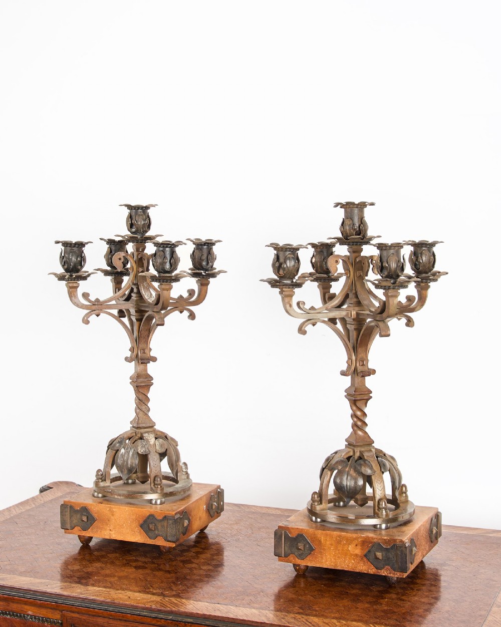 A pair of five-branch Gothic Revival metal candelabra featuring foliate cups, twisted columns, and wooden bases with iron strapwork. View IV