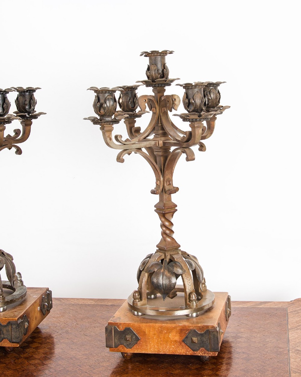 A pair of five-branch Gothic Revival metal candelabra featuring foliate cups, twisted columns, and wooden bases with iron strapwork. View VI