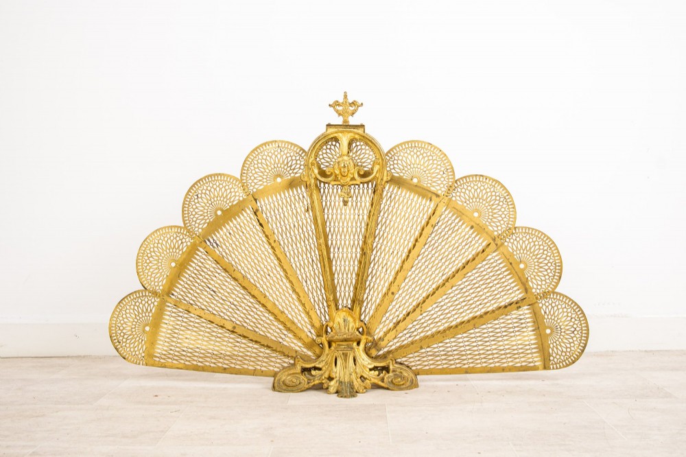 A French gilt brass peacock fan fire screen featuring pierced filigree blades unfolding from a central Rococo scroll base.