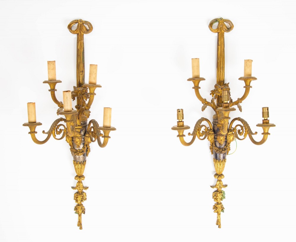A pair of French Louis XVI style gilt-bronze five-light wall sconces featuring ribbon bow tops, leaf motifs, and classical mask details.