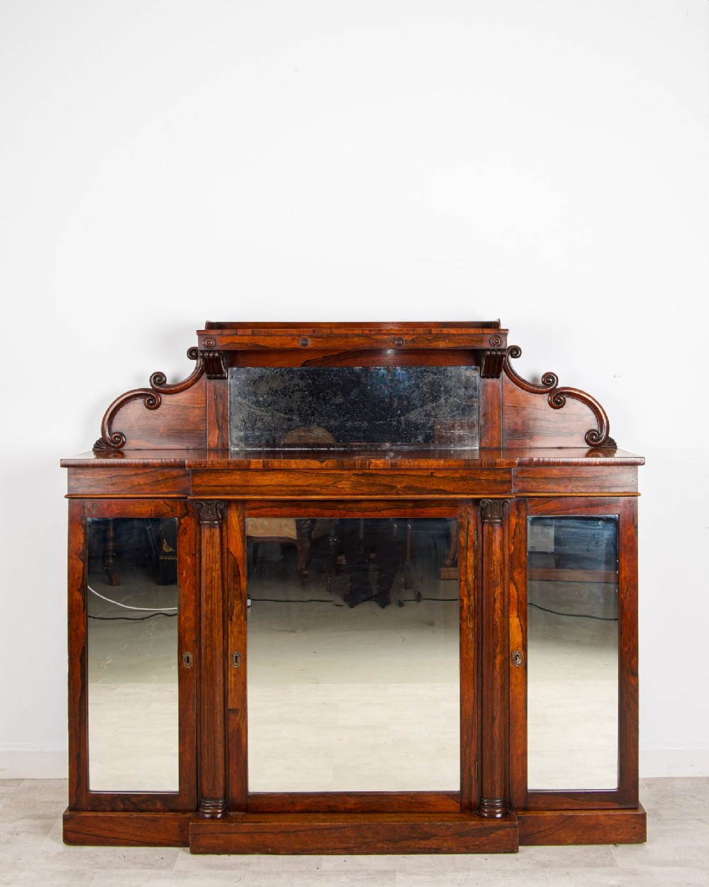 A Victorian rosewood side cabinet featuring a scroll-carved upper back with a shelf and mirror, positioned above three glass-panelled cupboard doors.