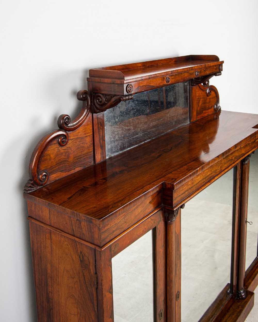 A Victorian rosewood side cabinet featuring a scroll-carved upper back with a shelf and mirror, positioned above three glass-panelled cupboard doors. View III
