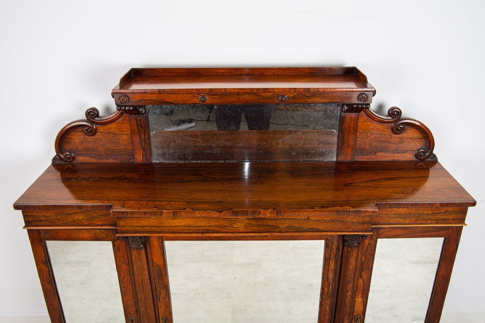A Victorian rosewood side cabinet featuring a scroll-carved upper back with a shelf and mirror, positioned above three glass-panelled cupboard doors. View V