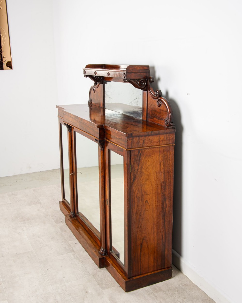 A Victorian rosewood side cabinet featuring a scroll-carved upper back with a shelf and mirror, positioned above three glass-panelled cupboard doors. View VII