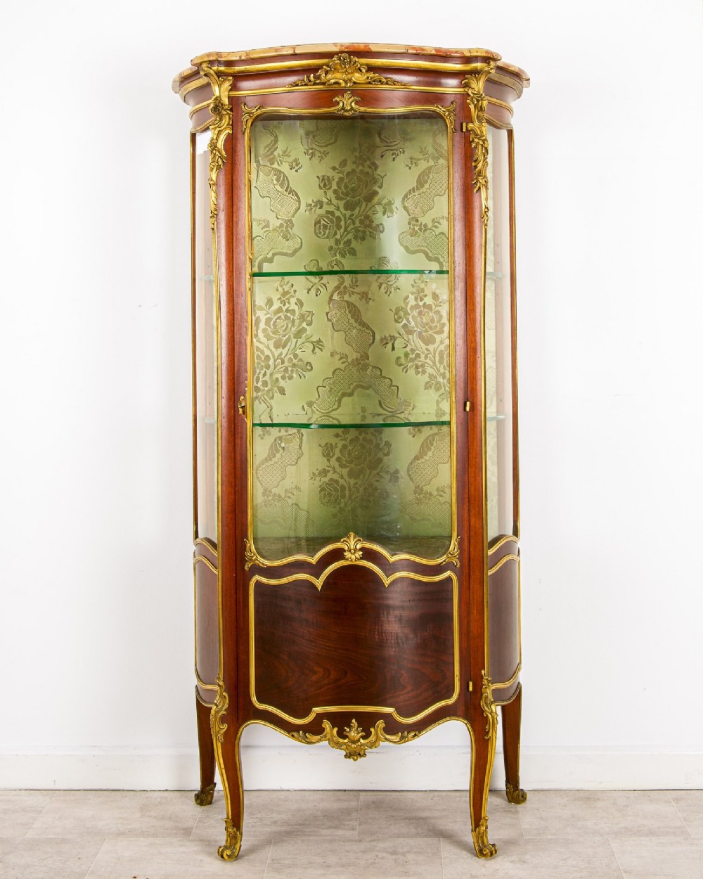An antique French Louis XV style vitrine cabinet featuring a marble top, glass panels, a fabric-lined interior with glass shelves, and gilt bronze mounts throughout.