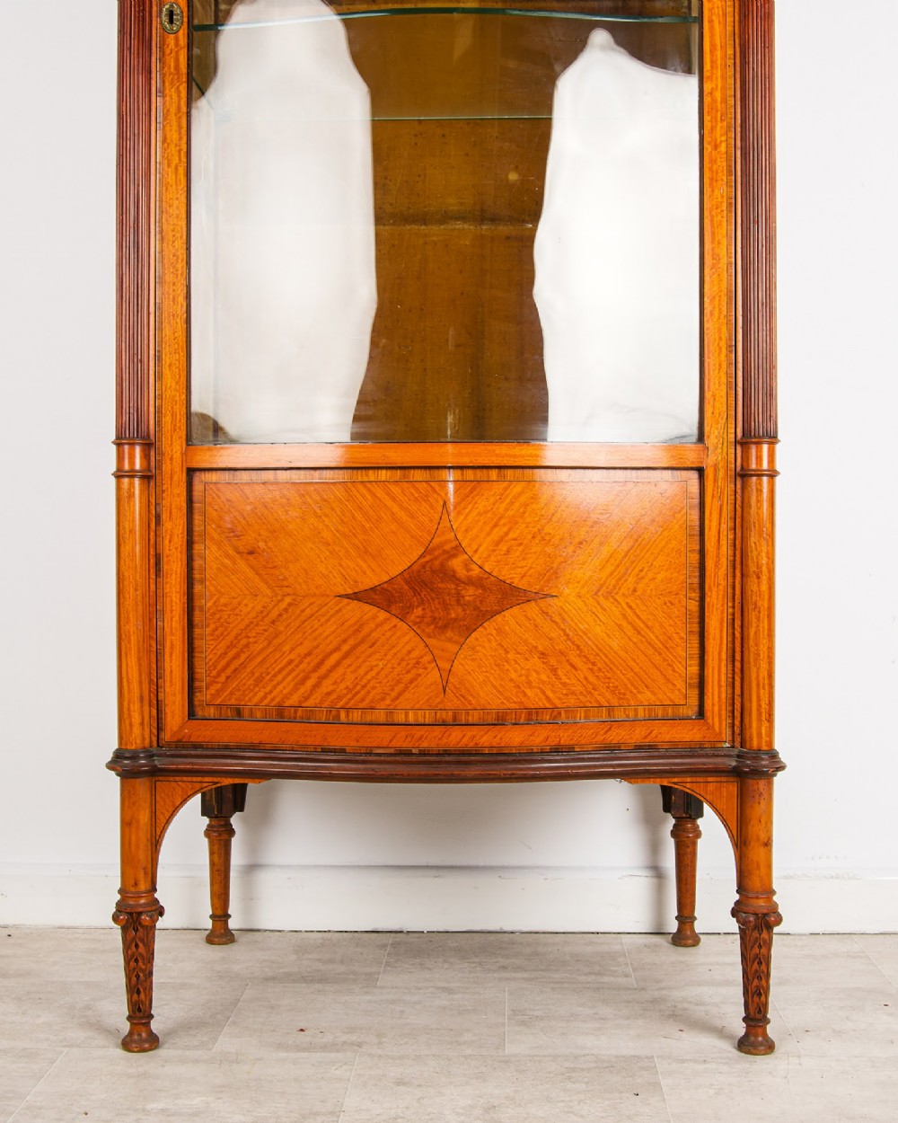 A tall Edwardian satinwood display cabinet featuring a curved glazed door, glass shelves, fluted corner columns, and geometric marquetry inlay. View V