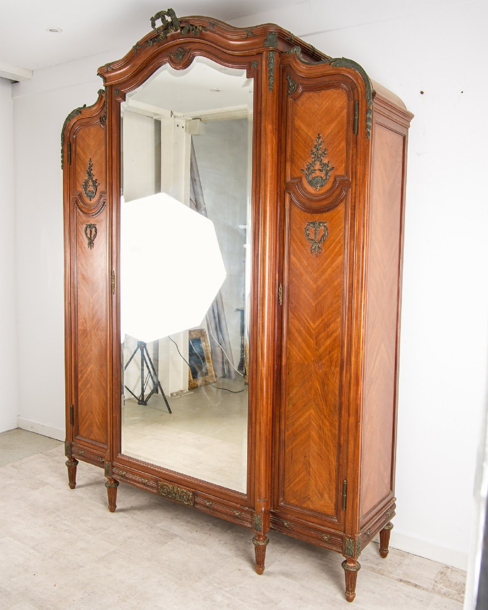 An antique French mahogany three-door armoire featuring a central arched mirrored door flanked by parquetry wood panels with gilt bronze ormolu mounts. View II