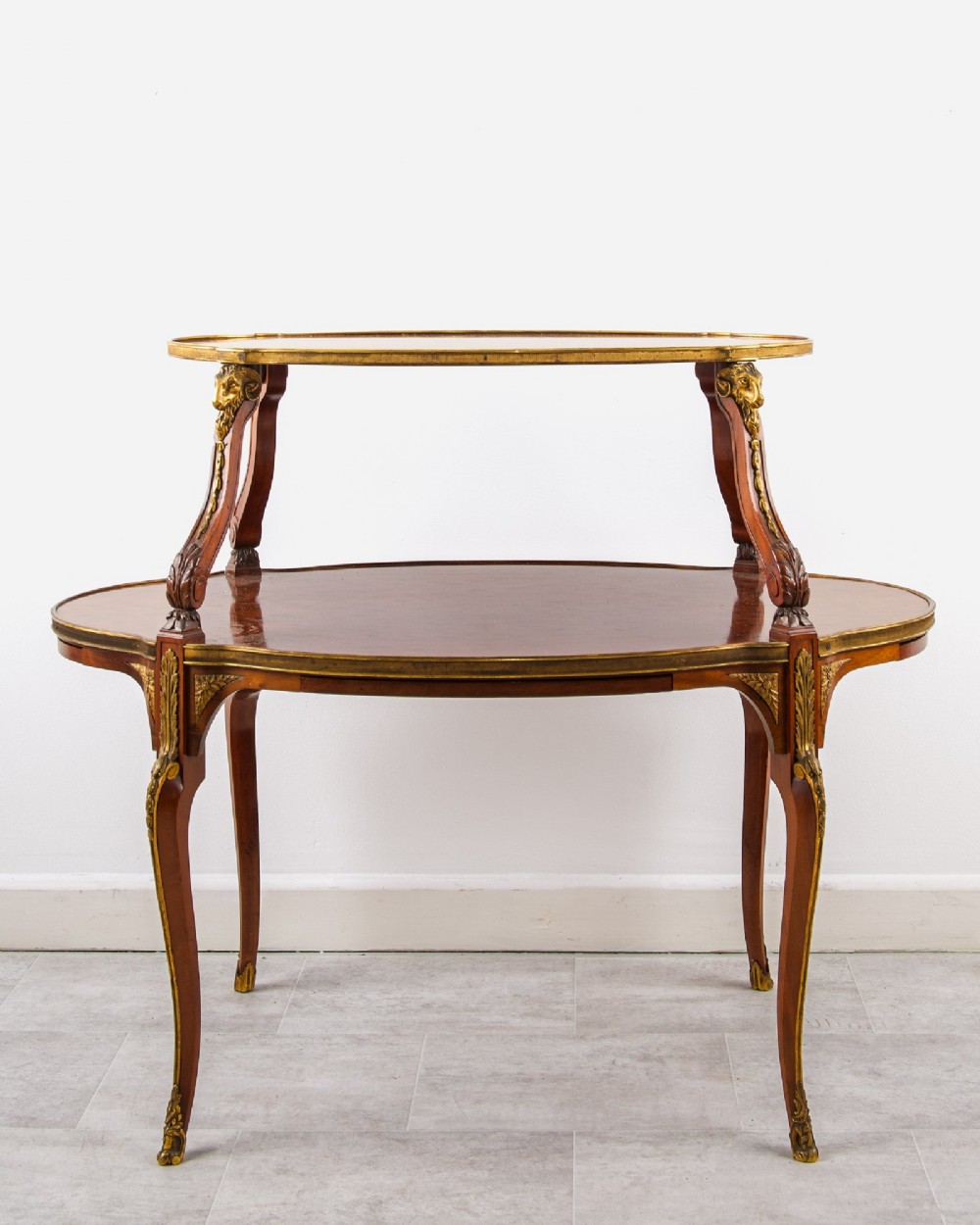 A two-tier French mahogany etagere centre table featuring oval surfaces, slender cabriole legs, and ornate gilded ormolu mounts.