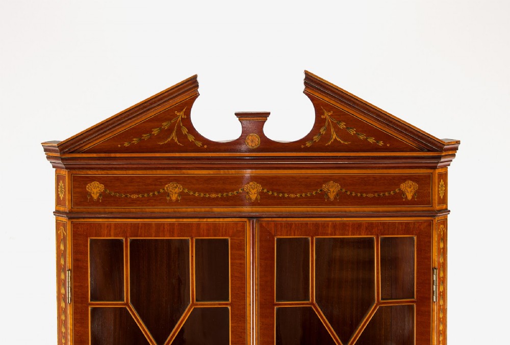 A tall Edwardian mahogany corner display cabinet featuring astragal glazed doors, a broken pediment, and classical inlaid oval panels on the lower doors. View V