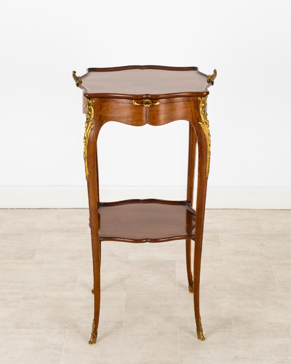 A French Louis XV style mahogany side table featuring gilt bronze mounts, cabriole legs, a serpentine upper top, and a lower tier shelf.