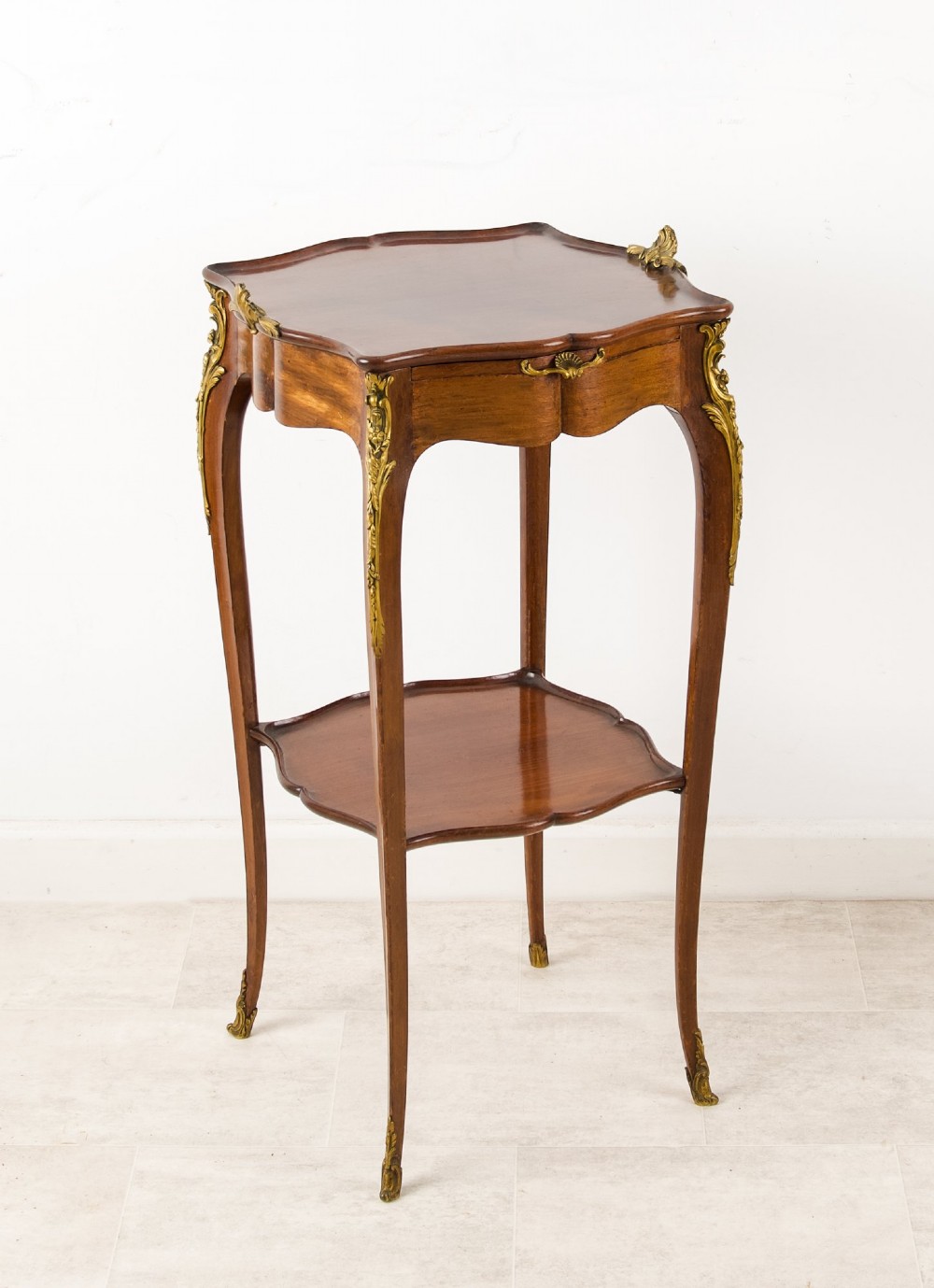 A French Louis XV style mahogany side table featuring gilt bronze mounts, cabriole legs, a serpentine upper top, and a lower tier shelf. View V