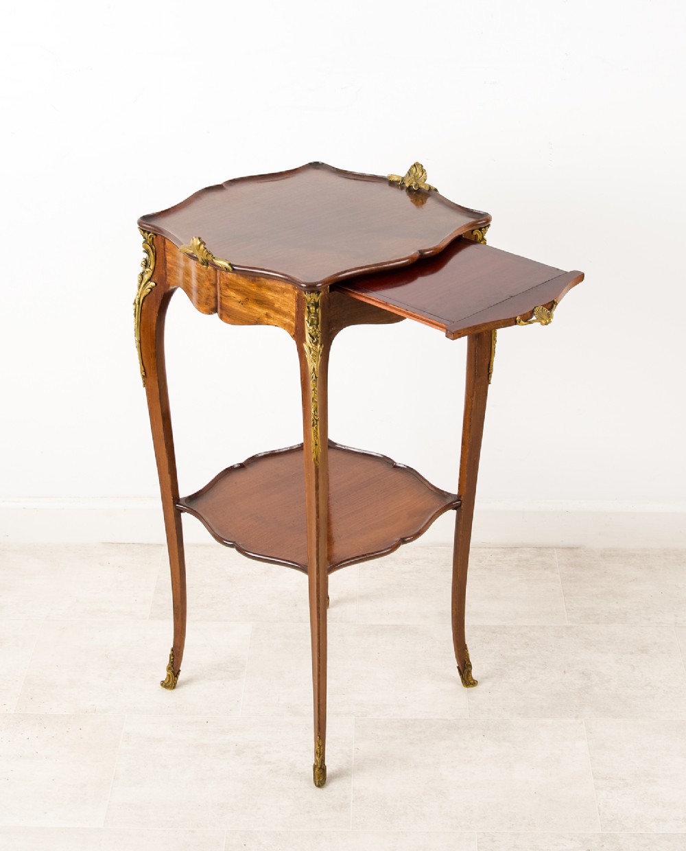 A French Louis XV style mahogany side table featuring gilt bronze mounts, cabriole legs, a serpentine upper top, and a lower tier shelf. View VI