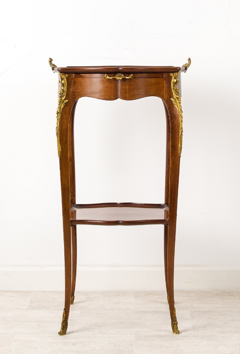 A French Louis XV style mahogany side table featuring gilt bronze mounts, cabriole legs, a serpentine upper top, and a lower tier shelf. View VII