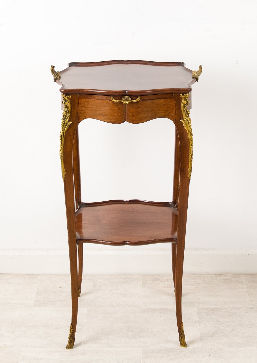 A French Louis XV style mahogany side table featuring gilt bronze mounts, cabriole legs, a serpentine upper top, and a lower tier shelf. View VIII