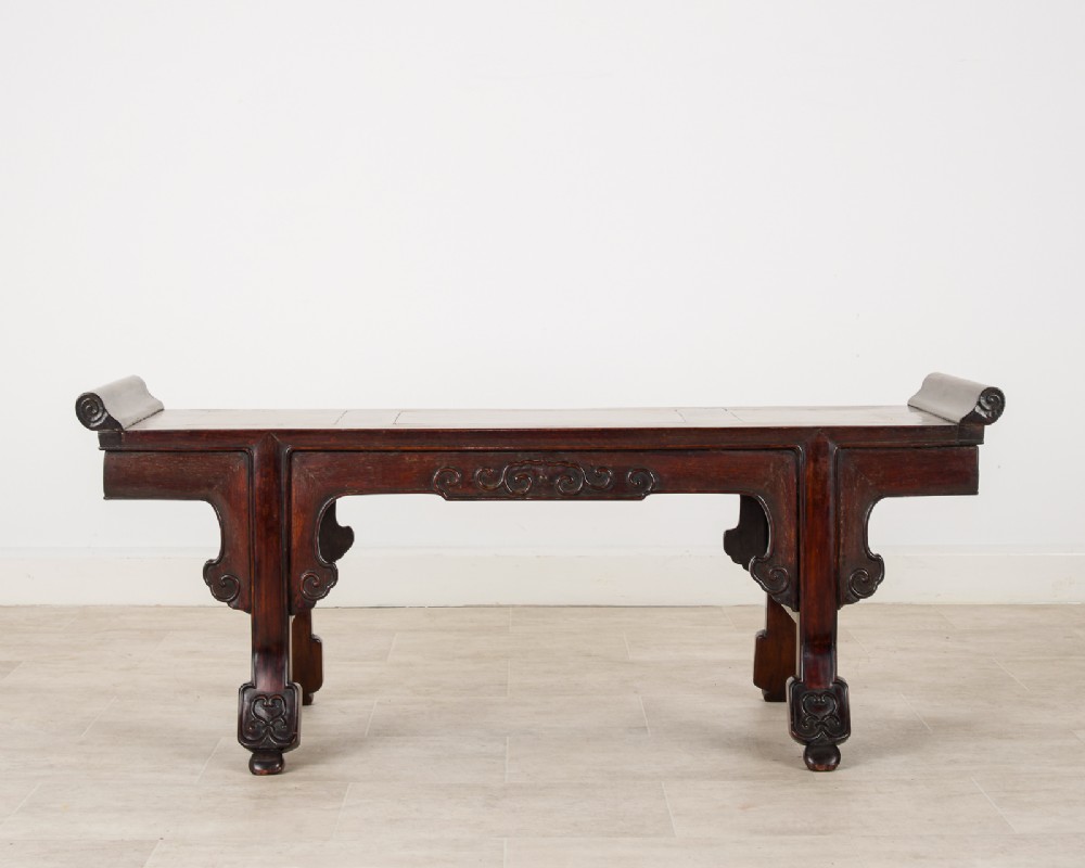 A nineteenth-century Chinese dark hardwood altar bench featuring raised scroll ends, a carved apron, and spandrels.