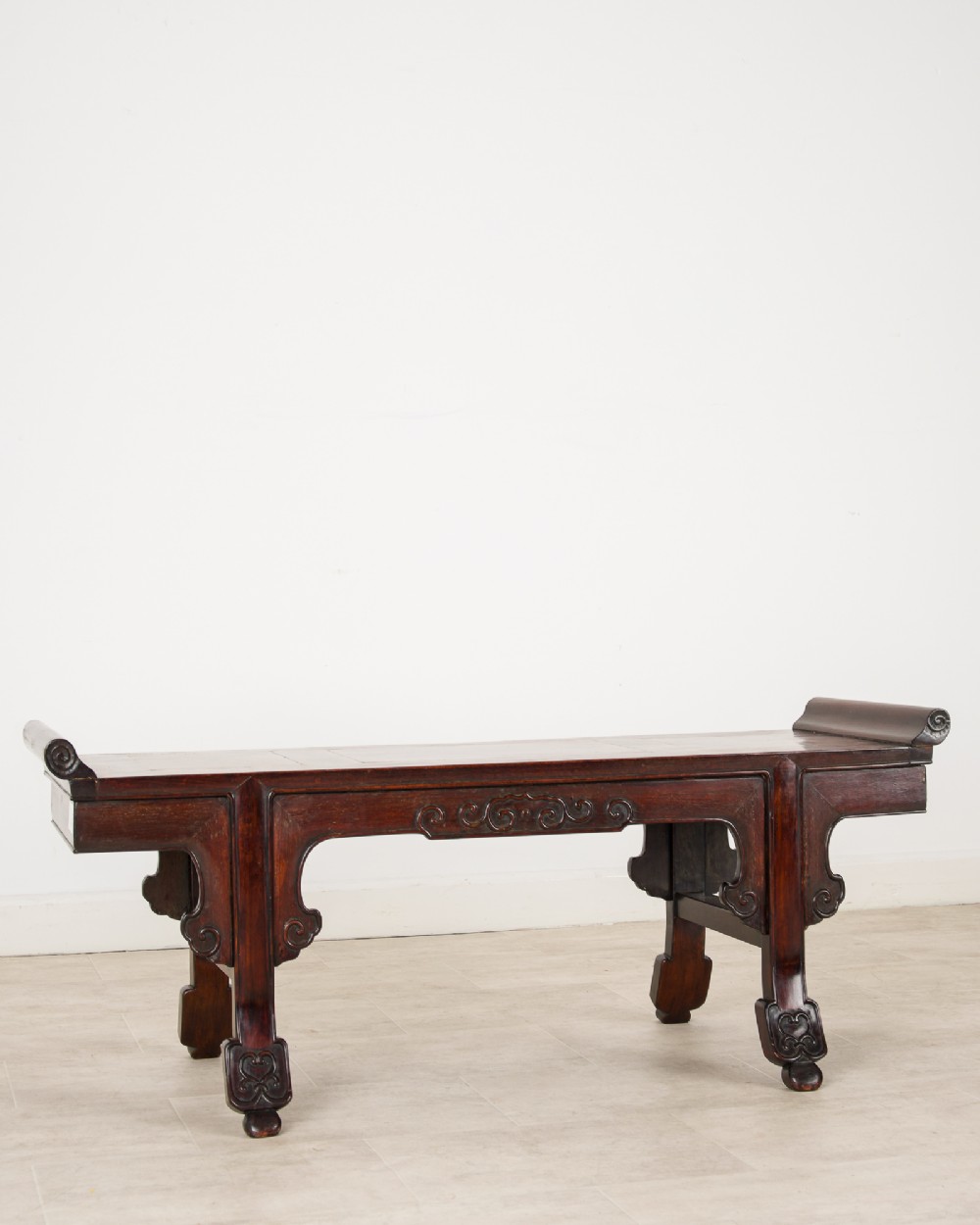 A nineteenth-century Chinese dark hardwood altar bench featuring raised scroll ends, a carved apron, and spandrels. View II