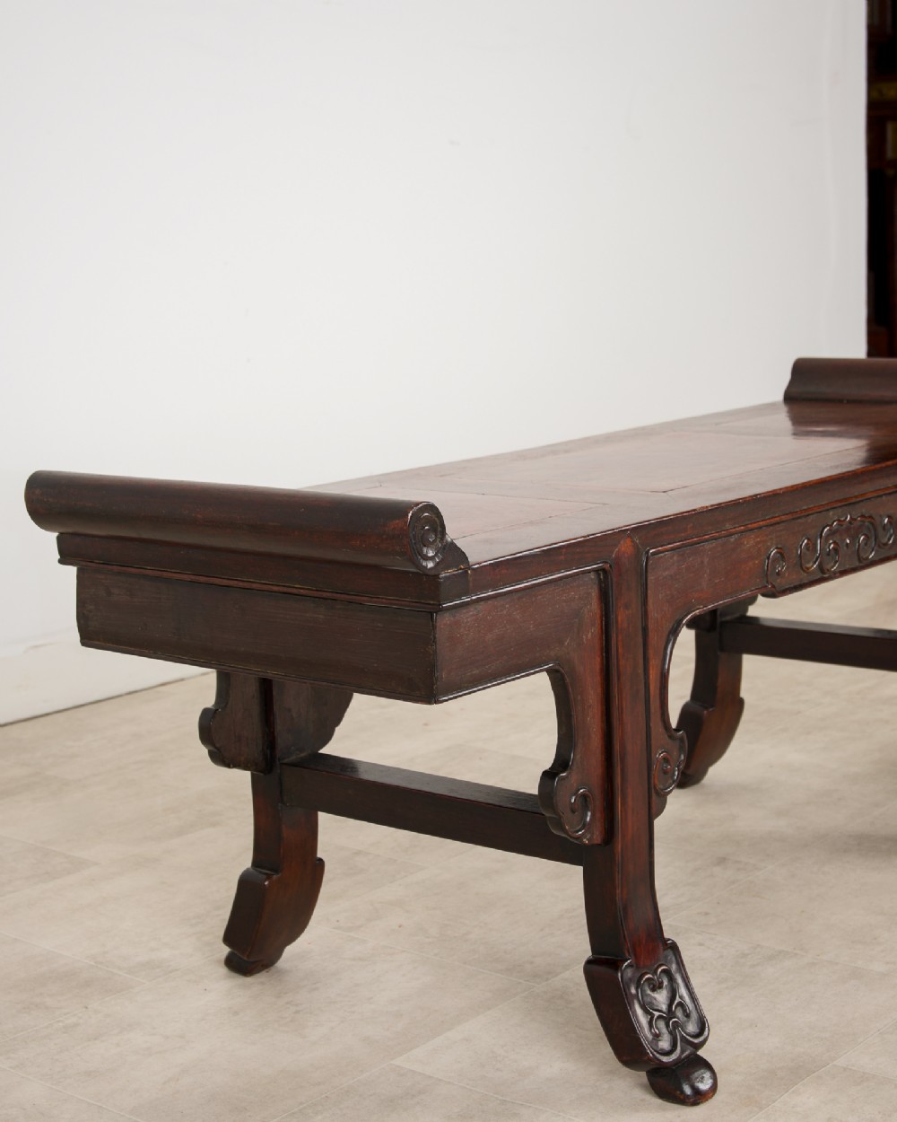 A nineteenth-century Chinese dark hardwood altar bench featuring raised scroll ends, a carved apron, and spandrels. View V