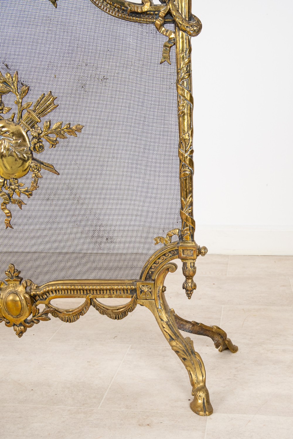 An antique French Louis XVI style gilt brass fire screen featuring a woven mesh panel decorated with a central trophy motif, ribbon bow cresting, and scrolled feet. View IV
