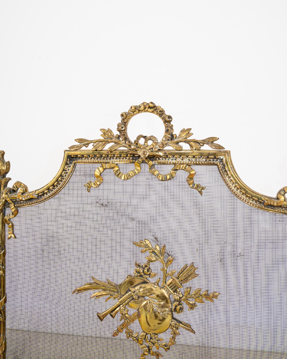 An antique French Louis XVI style gilt brass fire screen featuring a woven mesh panel decorated with a central trophy motif, ribbon bow cresting, and scrolled feet. View V
