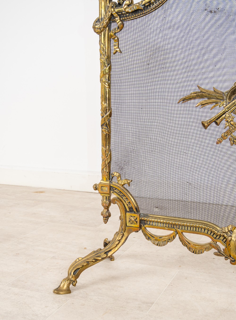 An antique French Louis XVI style gilt brass fire screen featuring a woven mesh panel decorated with a central trophy motif, ribbon bow cresting, and scrolled feet. View VI