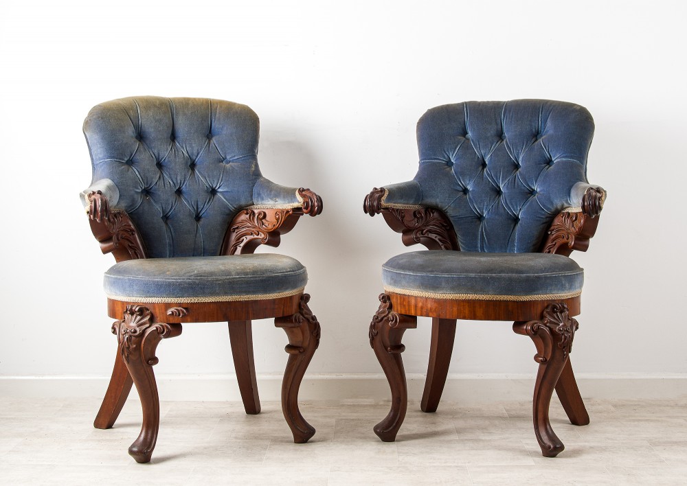 A pair of Victorian carved mahogany armchairs with button-backed blue velvet upholstery and detailed carved legs.